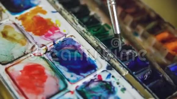 年轻的女艺术家用水彩画画图画特写刷子混合颜色在调色板视频的预览图