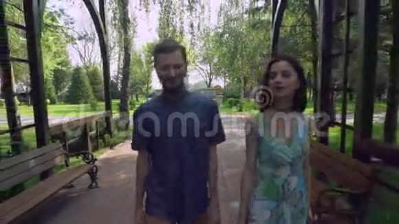 年轻夫妇走在拱门下公园的一条小路上聊天微笑视频的预览图