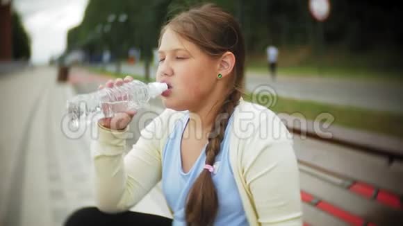 一个小胖女孩在滚筒上喝水一个孩子在长凳上的公园里喝水视频的预览图