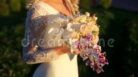 新娘用手在夕阳的明亮光线中抚摸着一束玫瑰和兰花视频的预览图