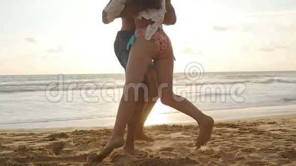 年轻夫妇在海滩上男人拥抱和旋转他的女人在日落女孩跳进男朋友的怀里他在旋转视频的预览图