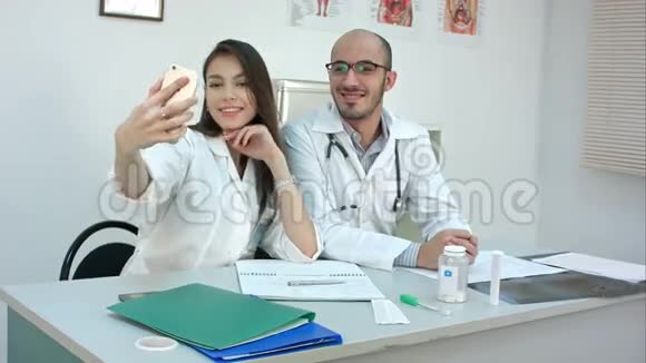 年轻的医生和漂亮的护士在办公桌前打电话自拍视频的预览图