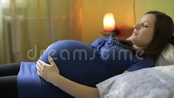 穿着蓝色连衣裙的孕妇躺在卧室里的一张床上放着红色的灯视频的预览图