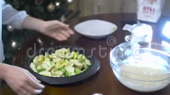 一个女人的手在烤盘上把糕点倒在苹果切片上视频的预览图