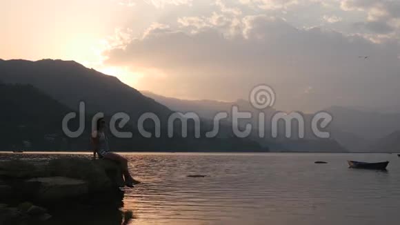 年轻的女士坐在湖边的一块岩石上视频的预览图