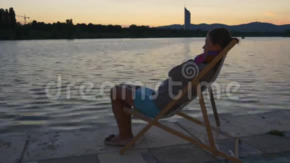 女人坐在夕阳下的河边视频的预览图