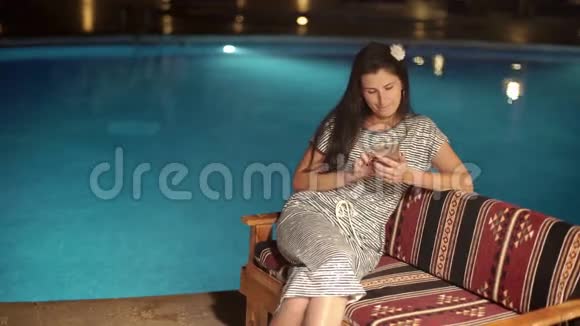 快乐女孩使用智能手机晚上在游泳池附近打字视频的预览图