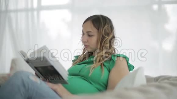 一位穿着绿色衬衫的孕妇坐在沙发上看书视频的预览图