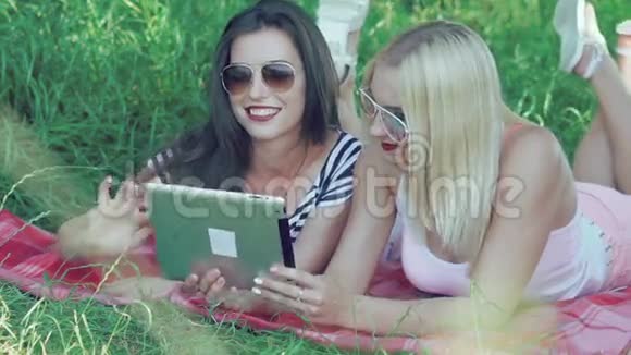 在阳光下的草地上躺着一台触摸屏平板电脑的女孩视频的预览图