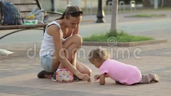 可爱的女孩和她的母亲在人行道上用粉笔画画视频的预览图