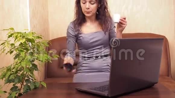 带着电话和咖啡的女孩一个穿着灰色连衣裙的女人在笔记本电脑后面带着手机在室内喝咖啡视频的预览图