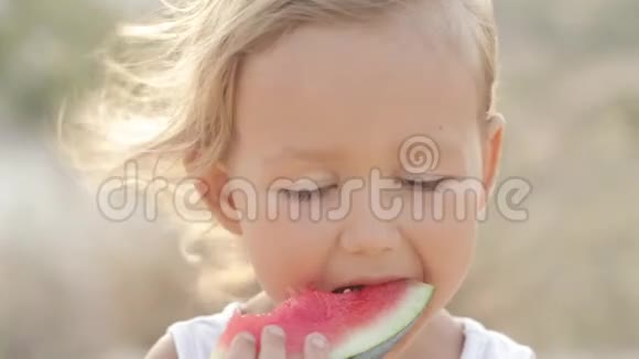 日出时小可爱小女孩吃红西瓜的特写镜头视频的预览图