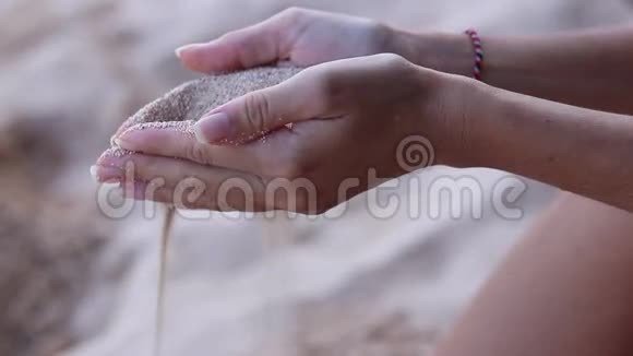 靠近女孩的手白色的沙子过滤她的手指而坐在海滩上印度尼西亚巴厘视频的预览图