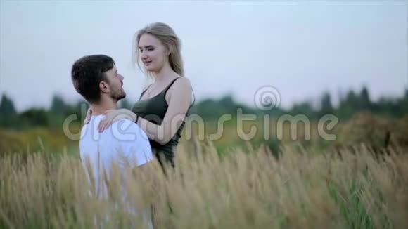 一对相爱的夫妻一个男人亲吻一个美丽的年轻女子并在日落或日出时把她举起来和她一起在田野上跳舞视频的预览图