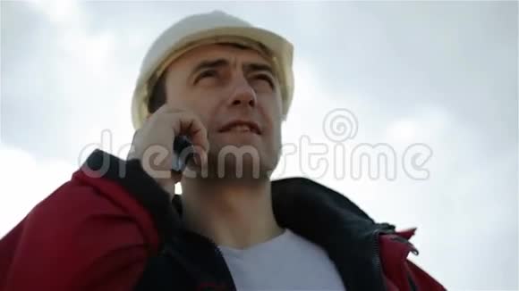 一个戴着白色头盔和红色夹克的建筑工人正在手机上交谈视频的预览图