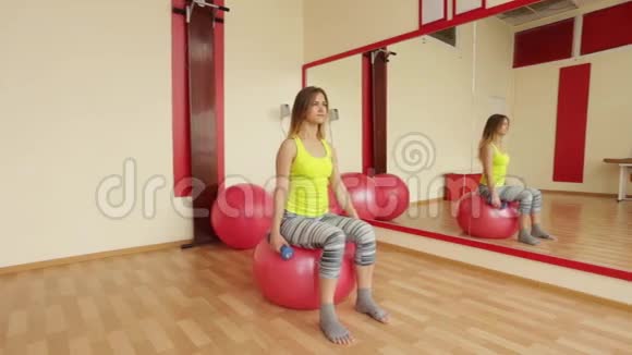 年轻女孩训练二头肌时使用哑铃而坐在一个健身球视频的预览图