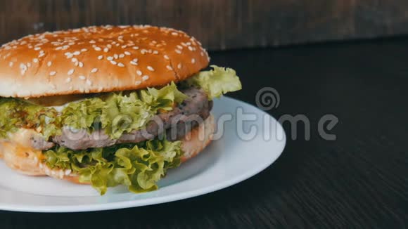 一个大的美味多汁的汉堡有三层切块新鲜生菜叶和奶酪放在一个时髦的白色盘子上视频的预览图