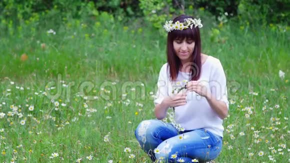 夏天在一片甘菊的草地上在一片森林里一个年轻的女人一个黑发的女人织着一个甘菊花圈视频的预览图