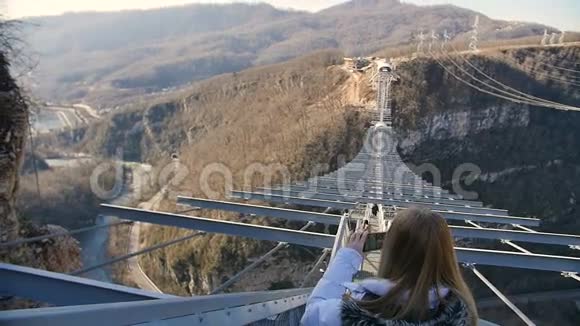 女人在峡谷上空的天空桥上拍摄自然风光视频的预览图