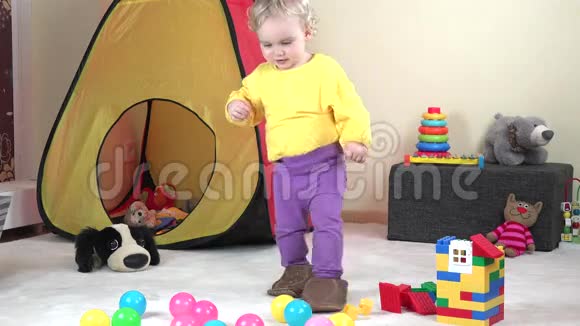 可爱的女婴和爸爸的大拖鞋在家里的玩具之间行走视频的预览图