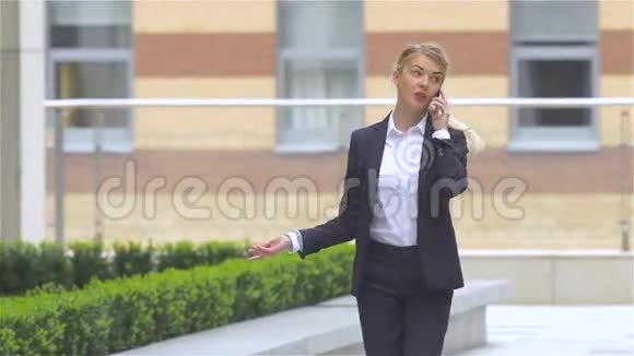 成功的金发女人在户外散步时用手机说话慢动作视频的预览图