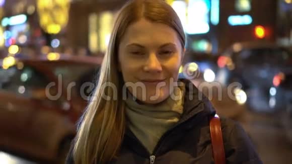 美丽迷人的年轻女子站在街上微笑城市灯光汽车经过视频的预览图