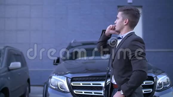 年轻的透视商人用手机交谈站在时尚的汽车旁边视频的预览图