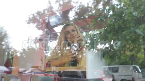 女孩在现代咖啡馆听音乐街上的交通在窗户反射视频的预览图