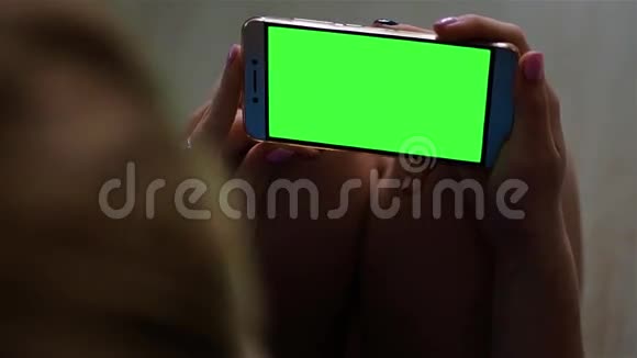金发少女手持一部智能手机在阳光下以景观模式显示绿色屏幕视频的预览图