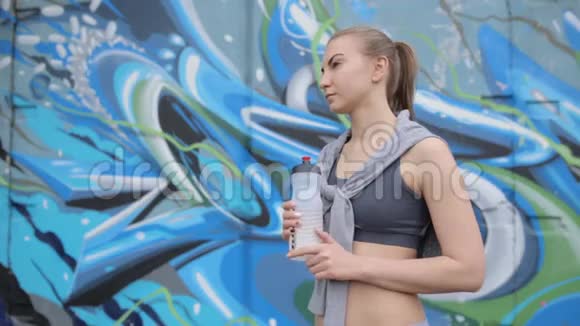 一个年轻的运动女孩在经过体重训练后手里握着一块蛋白质视频的预览图