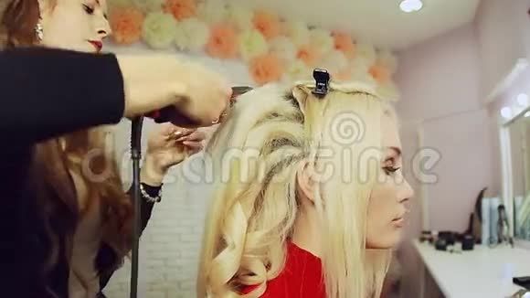使用卷发熨斗和卷发在金发女孩的头发上视频的预览图