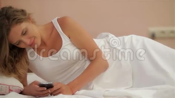 可爱的白种人女孩躺在床上用电话视频的预览图