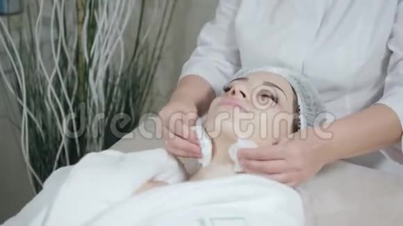用无菌餐巾纸脸擦拭年轻漂亮的女人在美容院接受治疗面部清洁泡沫使用视频的预览图