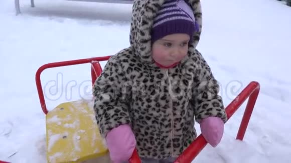 快乐的女婴在冬天的操场上玩秋千4K视频的预览图