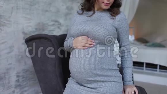 美丽的孕妇坐在扶手椅上双手放在肚子上女人穿着优雅的衣服美丽美丽视频的预览图