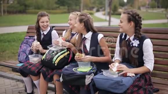 大学生在公园的长凳上吃三明治笑着说话快乐的年轻朋友一起吃饭视频的预览图