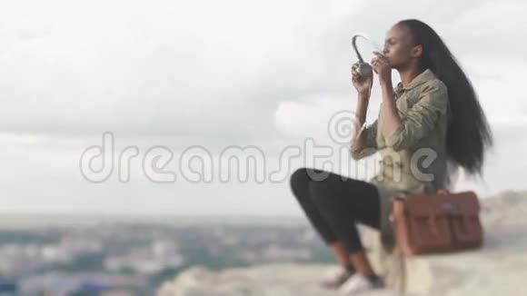 美丽的非裔美国年轻女子在蓝天和云彩背景下听音乐放松的时刻视频的预览图