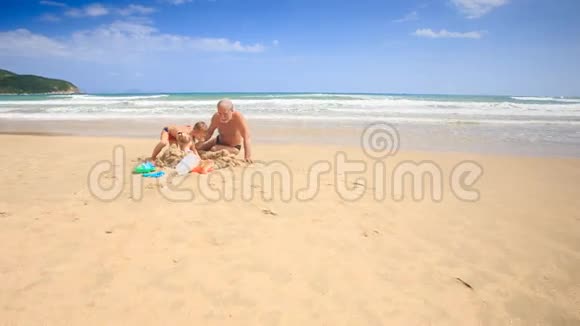镜头移动到爷爷的孩子在沙滩堆中玩耍视频的预览图