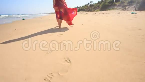 穿红色长裙的苗条女人在湿沙上留下脚印视频的预览图