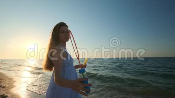 女孩在海滩上缓慢地吹泡泡傍晚日落时一个小女孩吹肥皂泡一路奔跑视频的预览图