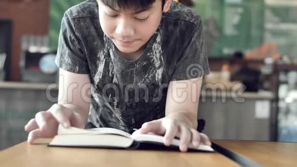 亚洲可爱的男孩一边看书一边等妈妈在咖啡馆买饮料视频的预览图
