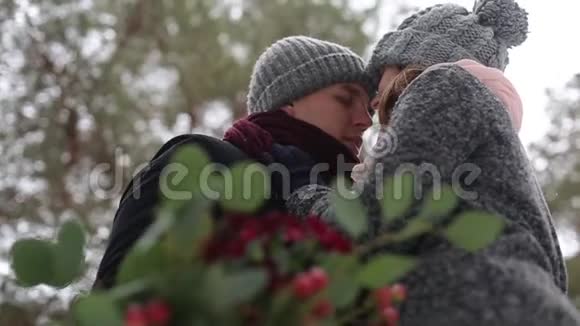 新婚夫妇新郎和新娘拥抱亲吻并在降雪期间在雪松林中温暖对方青年视频的预览图