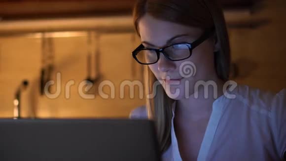 漂亮迷人的女人戴着眼镜在笔记本电脑上浏览互联网晚上厨房视频的预览图