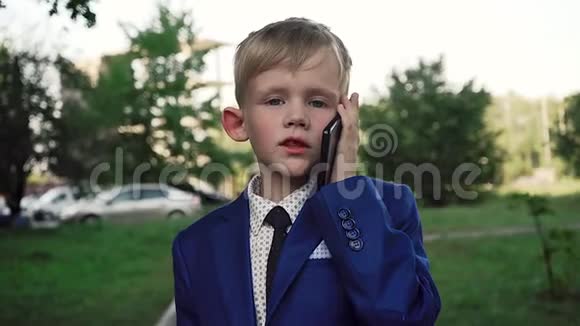 一个穿着西装脸严肃的小男孩正走在街上打着电话视频的预览图