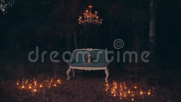 在黑暗的夏日森林里沙发上的婚礼花束照亮了点燃的蜡烛视频的预览图