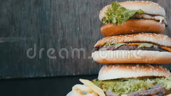 一盘炸薯条上有三个汉堡的大山汉堡包一个在另一个上面躺在一个时髦的木制上视频的预览图