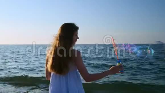 女孩在海滩上缓慢地吹泡泡傍晚日落时一个小女孩吹肥皂泡一路奔跑视频的预览图