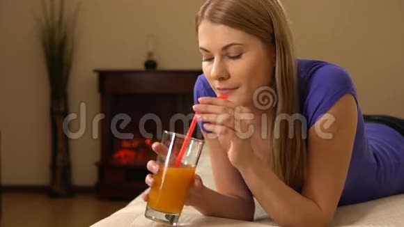 漂亮迷人的年轻女人躺在沙发上喝着杯子里的果汁视频的预览图