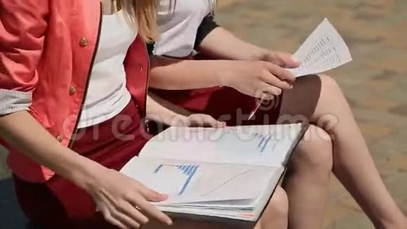 两个学生一起学习膝盖上有笔记坐在公园里特写镜头视频的预览图
