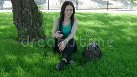 漂亮的女人坐在草地上拿着时尚的手提包看着相机视频的预览图